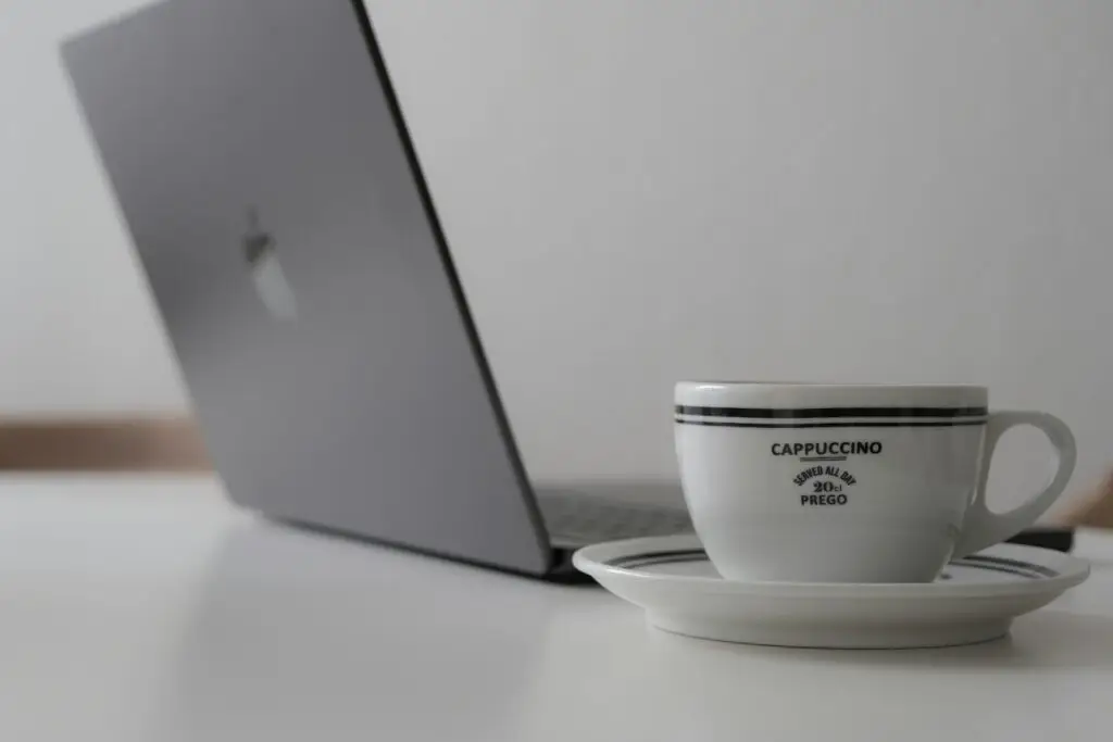 Un portátil y una taza de café sobre un escritorio blanco